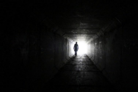 Picture of a person walking in tunnel with bright light at end