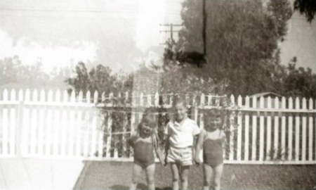 Photo of three small kids in front of white picked fence